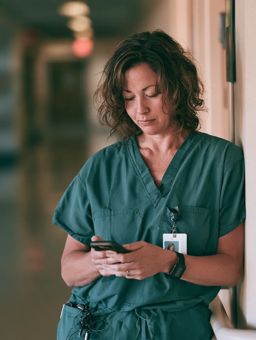 Nurse in scrubs checking emergency loan status on her phone during a hospital break